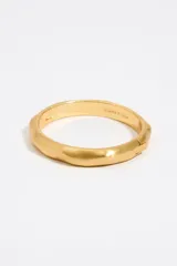Pulsera rígida dorada de metal con textura irregular y cierre de bisagra. Modelo personalizado con logo grabado.