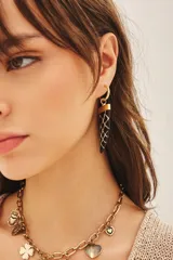 Aros colgantes con forma de cuerno, con base dorada y colgante negro con diseño geométrico blanco.