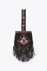 Bolso pequeño de mano con asa corta, confeccionado con abalorios negros y diseño floral bordado en tonos rosa y verde. Presenta flecos largos de abalorios en la parte inferior y cierre con botón a presión.
