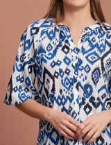 Blusa blanca de gasa marca Sioni, con cuello a la base y escote en V. Tiene abertura central con botones y mangas 3/4 con terminación fruncida.