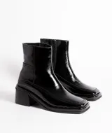 Bota corta de cuero charol negro, con caña baja, cierre lateral y taco cuadrado de madera.