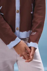 Cárdigan marrón de tejido de punto con cuello polo celeste, cierre frontal con botones y dos estrellas de mar bordadas.