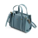 Cartera tote mini color celeste de cuero sintético con textura granulada. Tiene doble asa corta, correa larga regulable y extraíble, cierre superior y herrajes plateados. El frente está adornado con el logo metálico de la marca.