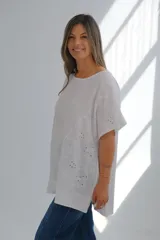 Blusa blanca de lino con cuello redondo, mangas cortas, bolsillo en el pecho y detalle de bordado calado en el lateral inferior. Corte holgado.