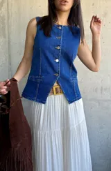 Chaleco de denim azul con escote en V y cierre frontal con botones. Tiene dos bolsillos frontales a la altura de la cintura.