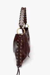 Bolso de hombro alargado color marrón oscuro, con detalle de pasados metálicos en los laterales y asa trenzada. Doble bolsillo interior con cremallera. Cierre mediante botón imantado.