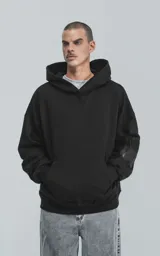 Hoodie negro de corte oversize con capucha, bolsillo tipo canguro y detalle de bolsillo con cierre en la manga izquierda.