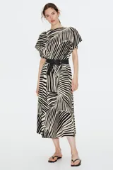 Vestido largo de punto con textura, estampado con motivos de hojas en blanco y negro. Tiene mangas cortas amplias, escote redondo y cintura entallada con pliegues.