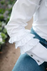 Camisa blanca de algodón con broderie, cuello alto con volados y mangas largas con puños abotonados y volados.
