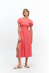 Vestido midi color coral, con cuello redondo, mangas cortas y corte evasé. Presenta detalle de punto panal elastizado en la zona del busto y tajos laterales.