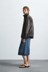 Cazadora bomber de efecto piel color marrón oscuro, con cuello solapa, cierre frontal de cremallera, bolsillos de vivo en cadera y bajo elástico.