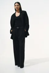 Pantalón sastrero negro de corte holgado con tiro alto y cierre con corchete y botón ocultos. Piernas amplias con pinzas, pliegues adelante y atrás, bolsillos al bies y bolsillos decorativos atrás.