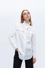 Camisa blanca de algodón con bordado calado, cuello alto con volados y cierre frontal con botones.