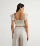 Blusa musculosa cropped color crudo, de algodón texturizado, con escote cuadrado, tirantes anchos con volantes y lastex en el dobladillo.