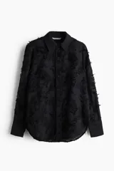 Camisa negra con textura, cuello clásico, abotonada al frente, canesú con pliegues en la espalda, mangas largas con puños abotonados y bajo redondeado.