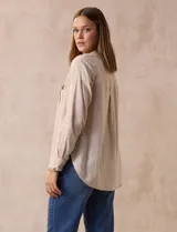 Blusa beige de lino y rayón, marca Dash. Tiene cuello a la base, escote en V y abertura con botones. Delantera con bolsillos. Largo de manga regulable con presilla y botón.