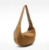 Bolso marrón de gamuza con forma de media luna y tachas plateadas. Tiene correa de hombro ajustable con hebilla metálica y cierre superior con cremallera.