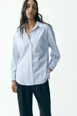 Camisa blanca con rayas verticales azul marino y lurex plateado, de corte recto, cuello solapa, escote en pico y cierre frontal con botones.