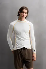 Camiseta de surf compresiva slim fit confeccionada en tejido técnico muy elástico y ligero. Con factor de protección ultravioleta 40+, cuello subido, manga larga, costuras planas y acabados combinados a contraste.