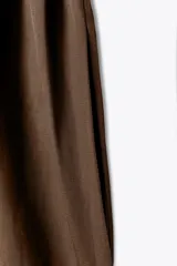 Vestido midi color marrón confeccionado en hilatura con mezcla de algodón y lino. Tiene cuello redondo, manga corta caída y detalle de pliegues en la cintura. Cierre en la espalda con abertura y botón.