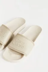 Ojotas de goma color beige con tira ancha sobre el empeine y logo de la marca en relieve.