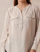 Blusa beige de lino y rayón, marca Dash. Tiene cuello a la base, escote en V y abertura con botones. Delantera con bolsillos. Largo de manga regulable con presilla y botón.