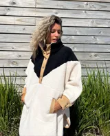 Buzo tipo poncho de polar color crudo con bloque superior en negro y detalles en beige.