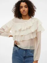 Blusa color crema con volados, cuello redondo y mangas largas con puños abotonados.