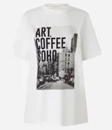 Remera blanca de algodón con cuello redondo y mangas cortas. Estampa fotográfica de una calle de Nueva York con texto "Art Coffee Soho".