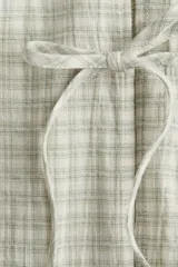 Vestido corto de algodón a cuadros en tonos beige y verde claro. Tiene cuello redondo con abertura y lazos, mangas cortas abullonadas y falda con leve vuelo.