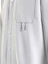 Camisa blanca de algodón con corte relaxed, manga larga, bolsillo en el pecho y logo de Calvin Klein Jeans estampado verticalmente en el frente.