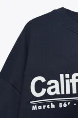 Sudadera azul marino de cuello redondo y manga larga, con texto "California" y diseño gráfico en blanco en el frente.