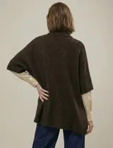 Capa o poncho tejido color verde esmeralda, con cuello polera alto que se cierra con un botón grande en el lateral. Presenta mangas cortas estilo japonesa y un calce amplio.