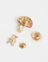 Set de tres prendedores dorados: un oso con strass, un hongo esmaltado rojo con lunares y una herradura con corazón.