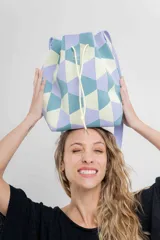 Bolso tipo bucket tejido con diseño geométrico en tonos lila, celeste y amarillo. Tiene cordón ajustable y correa ancha al tono para llevar al hombro o cruzado.