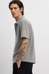 Camisa gris de manga corta en tejido piqué con cuello inglés, tapeta lisa, canesú en la espalda y bajo recto con aberturas laterales.