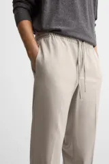 Pantalón color arena de corte recto, confeccionado en tejido elástico. Cuenta con cintura elástica ajustable con cordón, bolsillos laterales y bolsillos de vivo en la parte trasera.