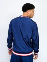 Buzo deportivo azul marino de nylon con cuello en V, puños y cintura acanalados con detalles tricolor (blanco, rojo y azul). Estampado frontal con la palabra "NACIONAL" en blanco y escudo del club C.N.de F. en el pecho. Corte clásico.