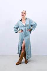 Vestido camisero largo celeste con bordado dorado de hojas, corte holgado, manga larga y cierre frontal con botones.