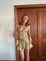 Vestido corto de lentejuelas color verde oliva, con escote en V, breteles finos cruzados en la espalda, cut-outs laterales y volado en el ruedo.