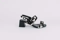 Sandalias de cuero con estampado animal print de vaca en blanco y negro, con detalles de tachas plateadas. Tienen correa trasera con hebilla y taco cuadrado de 5 cm.