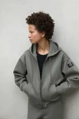 Campera gris con capucha ajustable con cordones, cierre frontal y bolsillos laterales.