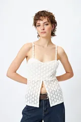 Top blanco de encaje con breteles finos, corte en la cintura y abertura frontal.