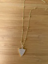 Collar dorado con dije en forma de escudo con incrustaciones de strass.