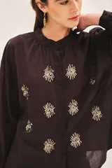 Camisa blanca de voilé de algodón con escote redondo y bordados de ojos en el delantero. De corte recto y mangas largas con puños abotonados.