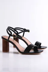 Sandalias de cuero negro con tacón cilíndrico de madera y tira fina con hebilla al tobillo.