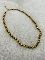 Collar corto de perlas doradas con hilo de seda azul marino y cierre de mosquetón dorado con cadena de extensión.