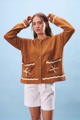 Cárdigan marrón de tejido de punto con cuello redondo y cierre frontal con botones. Tiene bolsillos frontales con diseño de olas y estrellas de mar en color blanco.