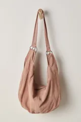 Bolso tipo hobo de gamuza color rosa pálido, con dos asas de hombro sujetas con argollas metálicas. Presenta un cierre principal con cremallera en la parte superior.