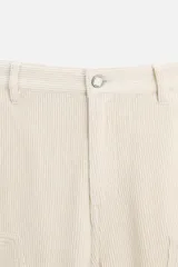 Pantalón de pana color crema, corte relaxed fit, con bolsillos frontales, bolsillos de parche en la parte trasera, bolsillos laterales en las piernas, trabilla multifunción y cierre con cremallera y botón.